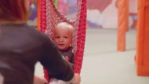 Back view of mother swinging her blond son in basket swing Stock Footage 83433260