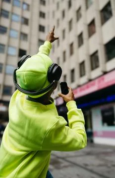 Back view of multiracial man in neon outfit pointing at sky with headphones.. Stock Photos