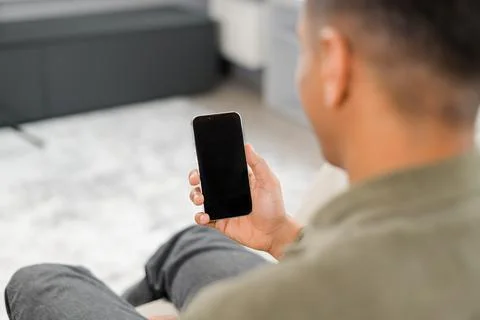 Back view of multiracial man sitting on sofa in office, using mobile phone for 写真素材