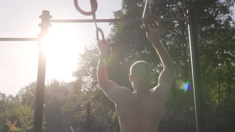Back view of a muscular young man training with gymnastic rings outdoors Stock Footage 287901714