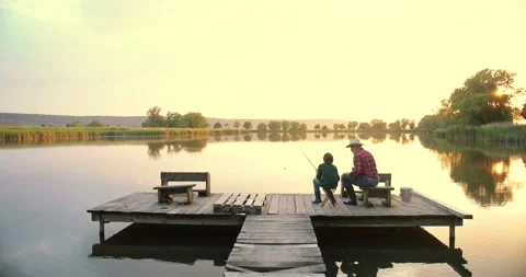Back view of the old grandfather in a hat fishing together with his grandson on Stock Footage 157821762