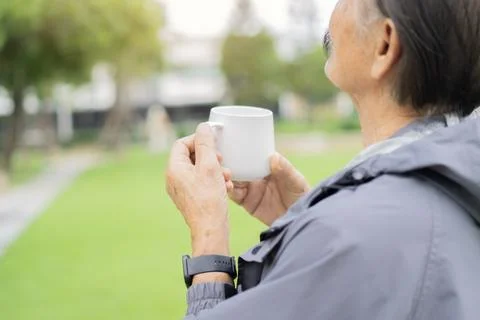 Back view of an old man with a beard holding a cup of coffee while standing.. Stock Photos