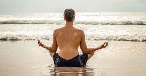 Back view of one man practicing yoga and meditates on the beach, ocean view.. Stock-Fotos