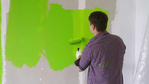 Back view of a painter in a checked shirt and gloves, painting over the wall Stock Footage 135925082