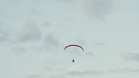 Back view of paraglider pilot flying under red canopy in cloudy sky Stock Footage 317159312