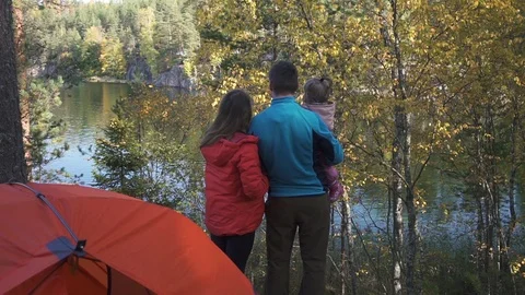 Back view of parents with kid standing in camping looking at lake in forest Stock Footage 119916997
