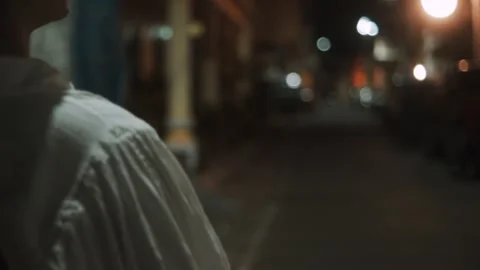 Back View of Person Walking on Dimly Lit Urban Street at Night with Hand Raised Stock Footage 340844722