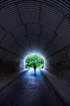 Back view of person walking through dark corrugated tunnel towards bright exi 写真素材