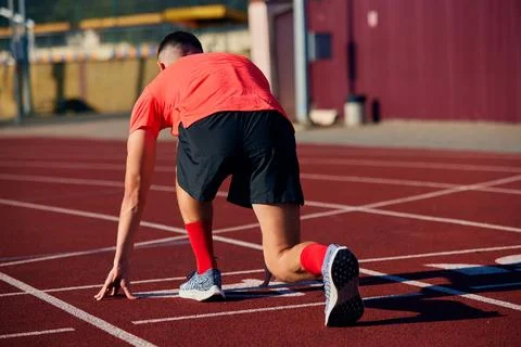 Back view photo of young man, ready to run standing on start line in low start Stock Photos