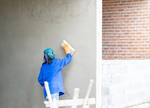 Back view of a plasterer finishing a grey concrete wall surface on a reside.. Stock Photos