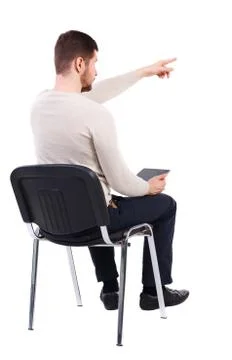 Back view of pointing man sitting on chair and looks at screen o Foto stock