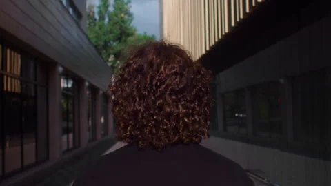 Back view portrait of a curly guy wearing black shirt walking at the city street Stock Footage 249999709