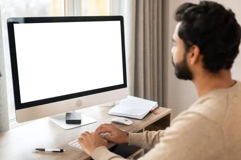 Back view of positive Hindi man in smart casual clothes using computer while Stock Photos
