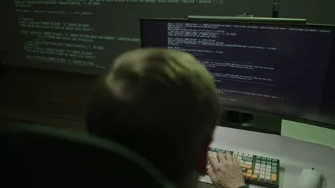 Back view of program developer sitting in dark room, working on computer and Stock Footage 324865837