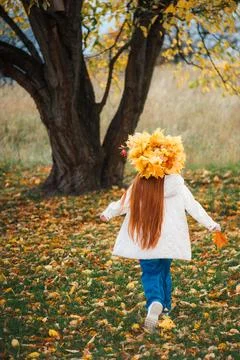 Back view of a red-haired child in a white jacket and maple leaf hat walkin.. Photos