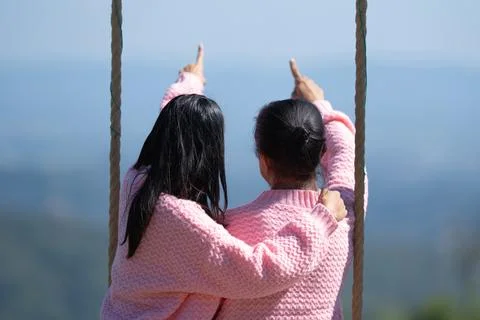 Back view of a romantic couple in matching pink sweaters sitting on a swing.. Foto stock