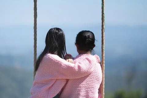 Back view of a romantic couple in matching pink sweaters sitting on a swing.. Stock Photos