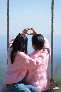 Back view of a romantic couple in matching pink sweaters sitting on a swing.. Stock Photos