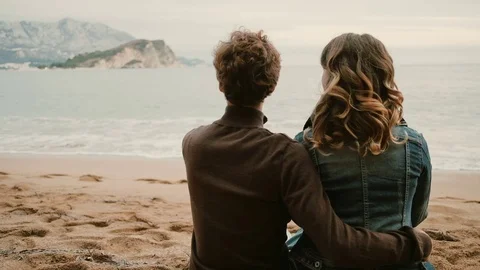 Back view of romantic couple sitting on the beach and look at the sea in autumn Stock Footage 82930751