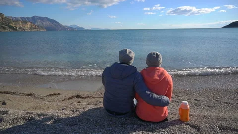Back view of romantic couple sitting on the beach and look at the sea Stock Footage 86105484