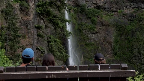 Back view of a romantic couple sitting on a bench and watching the water fall Stock Footage 245782266