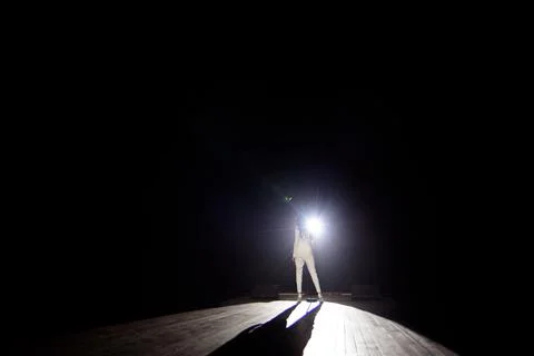Back view of a singer with microphone singing a song on stage in white lights. Stock Photos