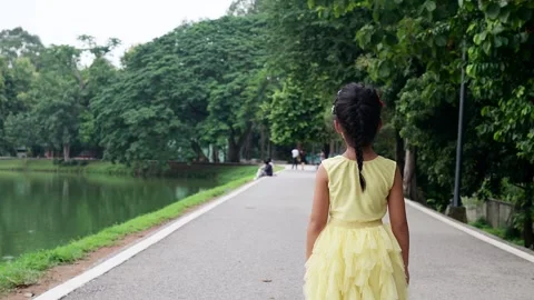 Back view small girl walking on the road in park. Stockbeeldmateriaal 247369264