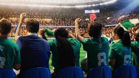 Back view of soccer crowd doing energetic chanting in stadium, holding beverages Stock Photos