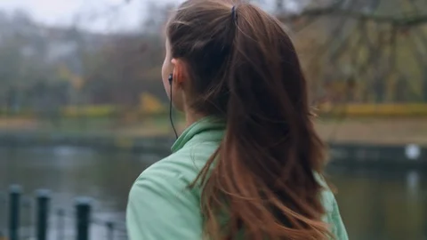 Back view of sporty girl in earphones running in autumn city park on riverside Stock Footage