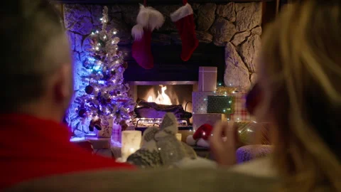 Back view of spouses relaxing at fireplace in room decorated for Merry Christmas Stock Footage 255316467