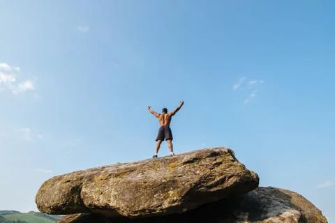 Back view of strong black bodybuilder posing on the rock against blue cloudy  Stock Photos