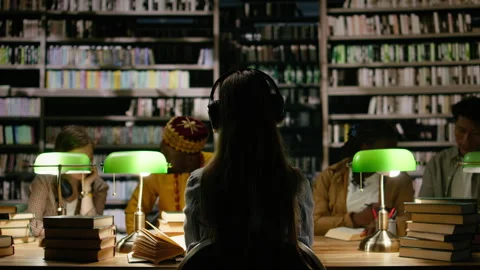 Back view of student adjusting headphones in dark library study room Stock Footage 337229995