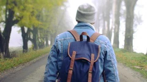 Back view of stylish hipster like man in jeans jacket with backpack walking down 스톡 동영상 108730621