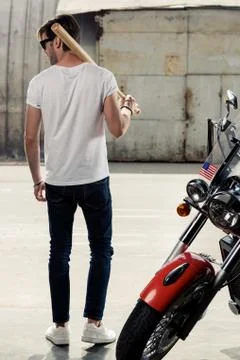 Back view of stylish young man with baseball bat on shoulder standing near mo 库存照片