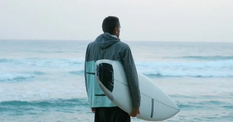 Back view of a surfer man with surfboard on the beach looking at Ocean waves. Stock Footage 162494355
