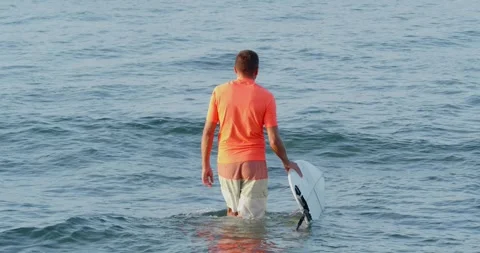 Back view of surfer walks in the ocean, holding surfboard in hand. Stock Footage 243600831
