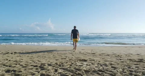 Back view of Surfer in yellow board shorts, takes surfboard goes to the ocean. Stock Footage 214516525