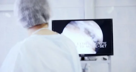 Back view of surgeon looks at monitors while preforming operation using surgical Video stock 121103986