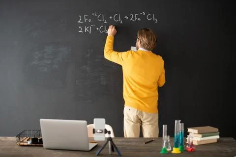 Back view of teacher of chemistry writing down chemical formula on blackboard Stock Photos