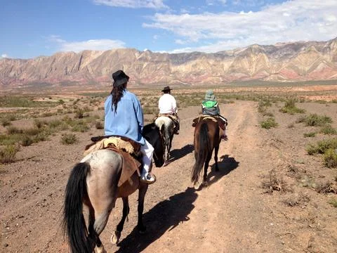 Back view of three people on horseback riding in desert scenery Stock Photos