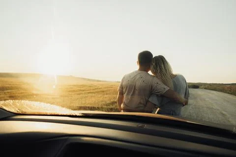 Back View Through Front Car Window on a Young Couple Hugging Near the Hood Stockfoto's