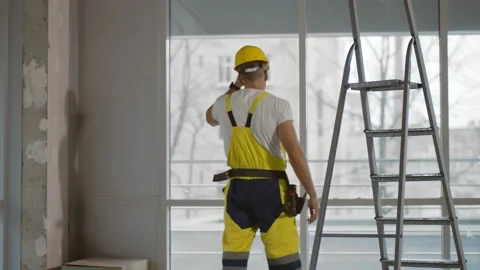 Back view of tired builder putting off hardhat and looking out of window at Stock Footage 145970056