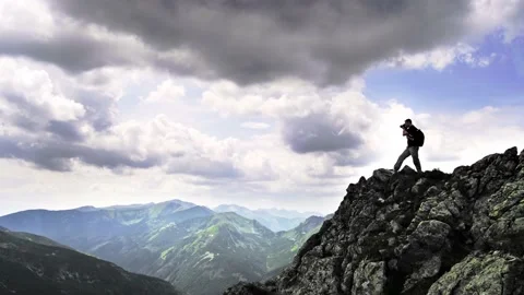 Back view of a tourist, standing on the edge of a high mountain and take a photo Video stock 158007262