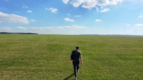 Back view of a tourist walking through a huge green meadow under a blue sky Stock Footage 287249014