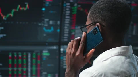 Back view of trader looking at multiple computer monitors with data and talking 스톡 동영상 193638380