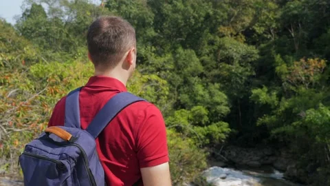Back view of travel man with backpack standing on rock and looking on river Видео 171078454