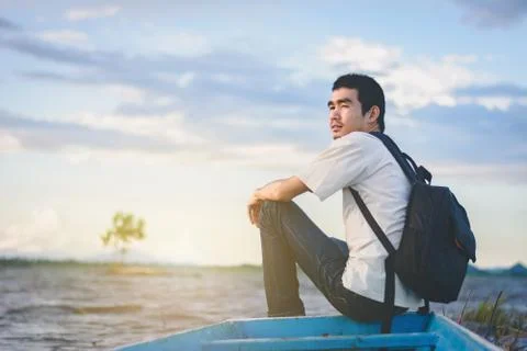 Back view of Travel man with backpack sitting on tail of the boat with lake a Stock-Fotos