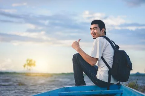 Back view of Travel man with backpack sitting on tail of the boat with lake a Stock Photos