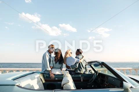 Back view of two couples standing and hugging near car Stock Photos