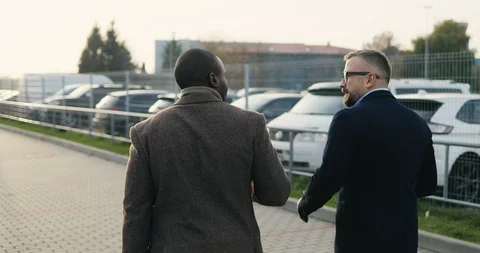 Back view on the two multiethnical stylish businessmen walking at the parking Stock Footage 100447842